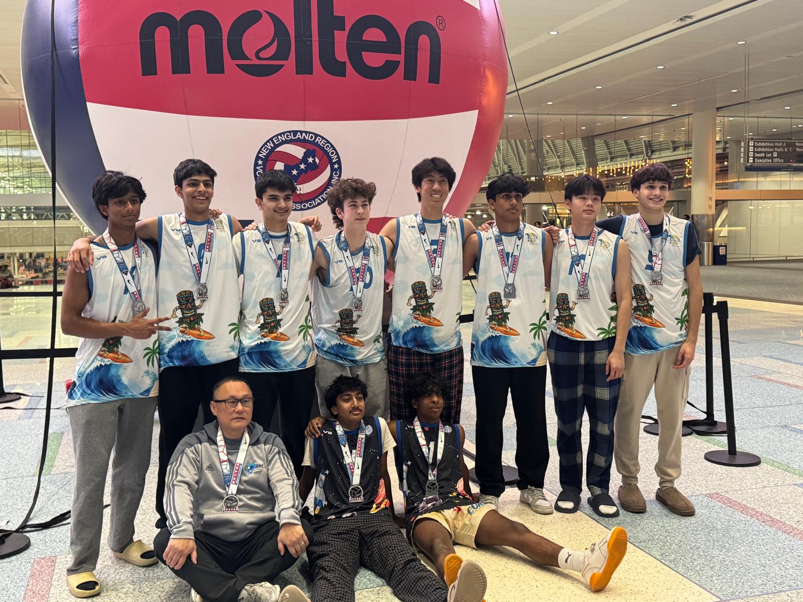 The Core team and their coach posing with medals in front of a giant inflatable Molten volleyball