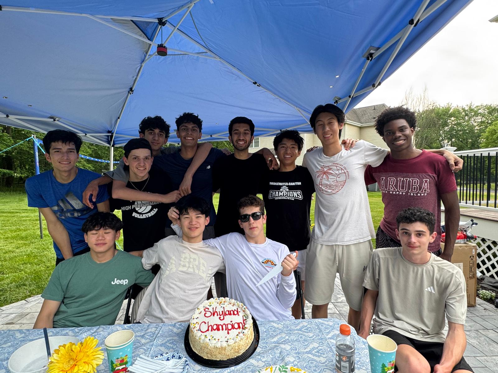 The team gathered under a blue canopy around a cake reading Skyland Champion!